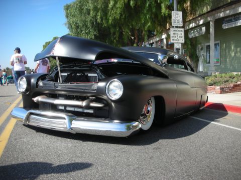 1998 Ford Crown Victoria - A customized black hot rod with its hood open sits on a street, displaying its chrome bumper and whitewall tires.