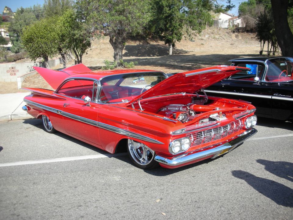 Red 1959 Chevrolet Impala hardtop with hood open at outdoor car show