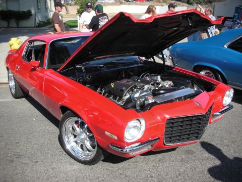 1998 Ford Crown Victoria - A red coupe from the 1970s is displayed with its hood open, revealing a custom engine and chrome wheels.