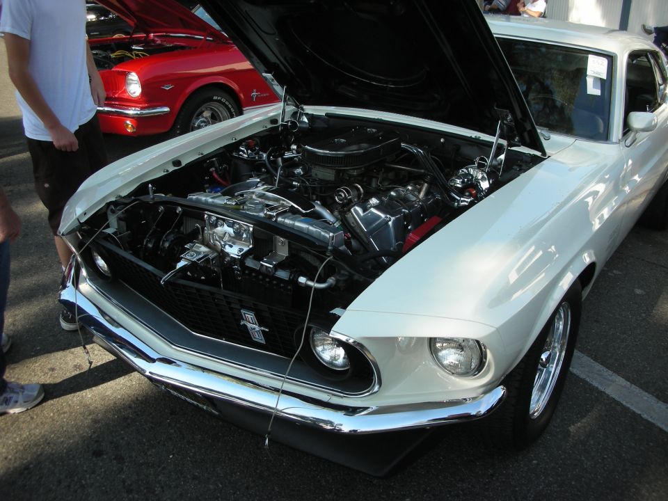 White 1969 Ford Mustang with hood open showing engine at car show