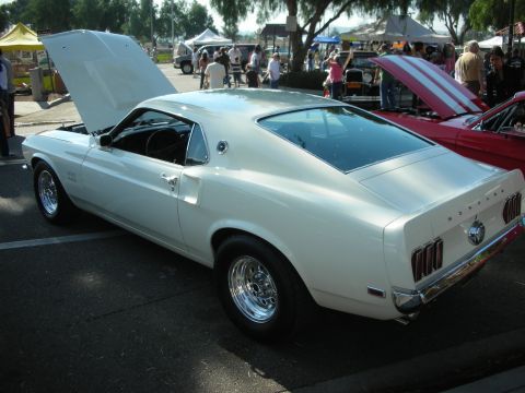 1998 Ford Crown Victoria - A white 1969 Ford Mustang coupe is parked with its hood open at an outdoor event.