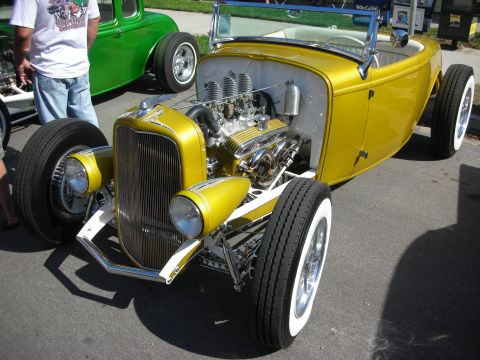 1998 Ford Crown Victoria - A custom yellow roadster with a powerful engine is parked next to a green coupe.