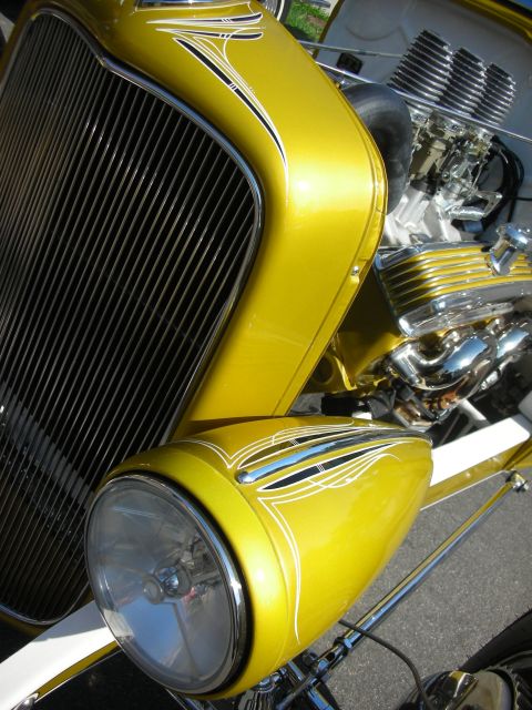 1998 Ford Crown Victoria - A yellow hot rod with a prominent chrome grille and custom pinstripe artwork on its front end.