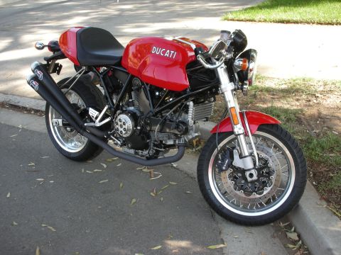 1998 Ford Crown Victoria - A red Ducati motorcycle is parked on the side of the road, showing its engine and dual exhaust pipes.