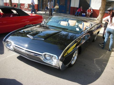 1998 Ford Crown Victoria - A shiny black convertible is parked on a street next to a red convertible, with people watching from the sidewalk.