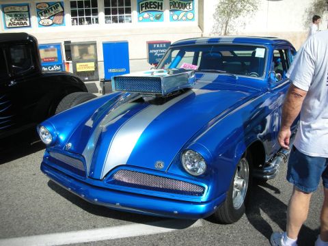 1998 Ford Crown Victoria - A customized blue hot rod with silver stripes and a large hood scoop is parked next to another vehicle.