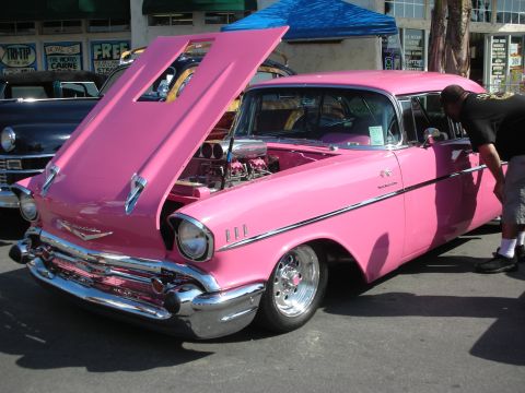 1998 Ford Crown Victoria - A man inspects a bright pink 1957 Chevrolet Bel Air with its hood raised, revealing a powerful engine.