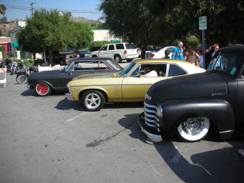 1998 Ford Crown Victoria - A trio of vintage American cars, including a black pickup truck and two coupes, are parked side-by-side in a sunny outdoor lot.