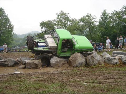 1978 Ford Bronco - This modified green off-road vehicle is stuck on a rocky obstacle course with spectators watching.