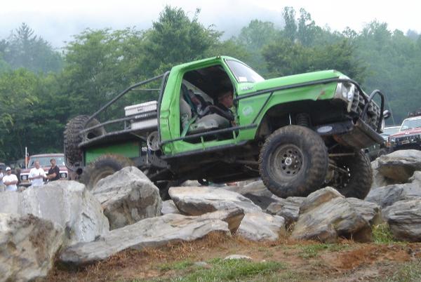Green doorless Ford 4x4 with roll cage crawling over boulders at an off-road event
