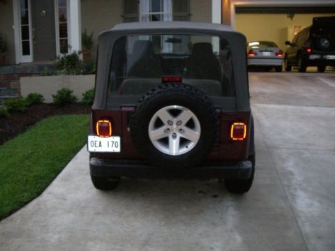 1995 Ford Bronco - A maroon Jeep Wrangler is parked in a driveway, with other vehicles visible in the background.