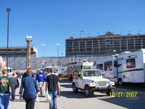 1979 Ford F-150 - A white Jeep Wrangler and an RV are parked in front of a grandstand at a racetrack on a sunny day.