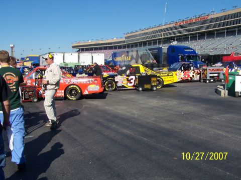 1979 Ford F-150 - Race trucks are lined up at Atlanta Motor Speedway on a sunny day, with spectators in the stands.
