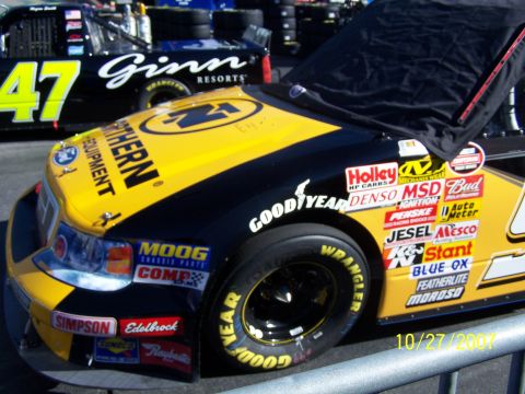 1979 Ford F-150 - A race car with numerous sponsor decals sits covered, with another car visible in the background.
