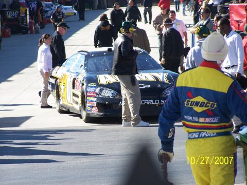 1979 Ford F-150 - A black and yellow Chevrolet race car is parked on the track, surrounded by crew members and spectators.