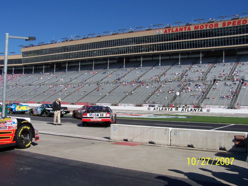 Race cars lined up on a track with grandstands in the background
