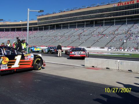 1979 Ford F-150 - Multiple NASCAR race cars are staged on the track at Atlanta Motor Speedway, with spectators in the stands.