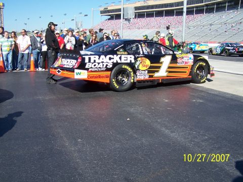1979 Ford F-150 - A NASCAR race car is parked on pit road with spectators and other race cars visible in the background.