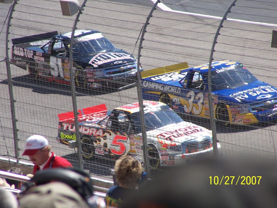 Three NASCAR trucks racing on a track. The trucks are numbered 5, 33, and 51. The date 10/27/2007 is visible