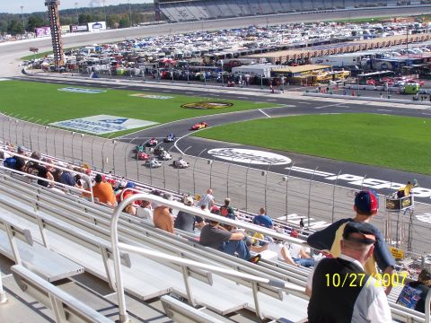1979 Ford F-150 - Spectators watch race cars on the track at a speedway, with many vehicles parked in the background.
