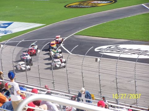 1979 Ford F-150 - Several stock cars are racing on a track, viewed from the stands with spectators present.