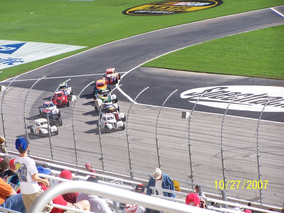stock cars racing on a track, with spectators in the foreground