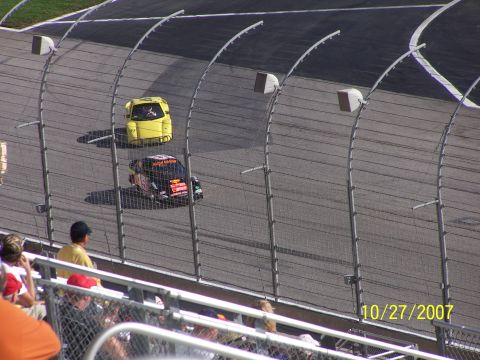 1979 Ford F-150 - A yellow car and a black and orange race car are seen on the track, with spectators in the foreground.