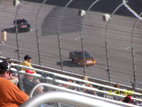 1979 Ford F-150 - Two stock cars race on a track while spectators watch from the stands.
