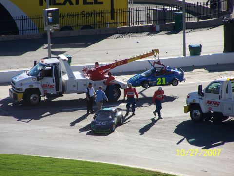 1979 Ford F-150 - Race cars are being towed off the track by tow trucks, with crew members supervising the operation.
