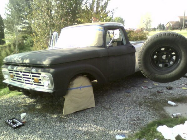 Early-1960s Ford pickup partly sprayed flat black with masked wheel on a gravel driveway