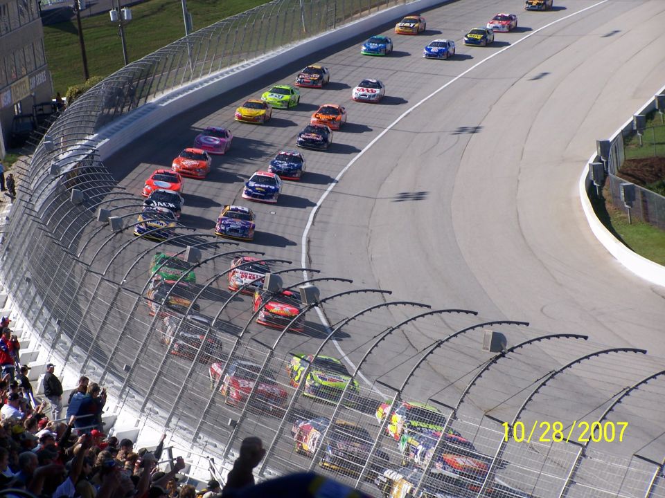 Stock cars racing on a track, with spectators in the foreground. The date 10/28/2007 is visible