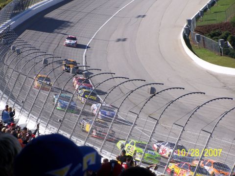 1979 Ford F-150 - Multiple race cars compete on a track, viewed from above with spectators present.