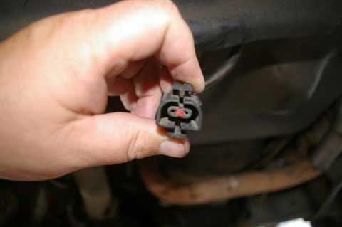 1986 Ford Bronco - Close-up of a hand holding a vehicle electrical connector, showing its internal contacts.
