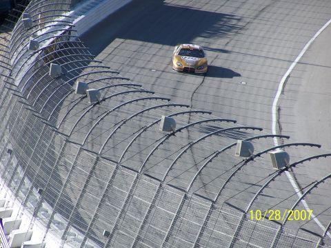 1979 Ford F-150 - A gold race car drives on a track, seen from above and behind a fence.