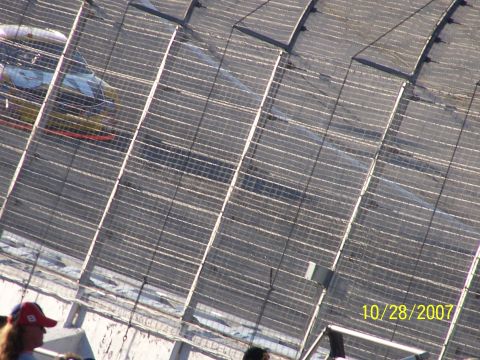 1979 Ford F-150 - A race car speeds around a track, viewed from an elevated position behind a safety fence.