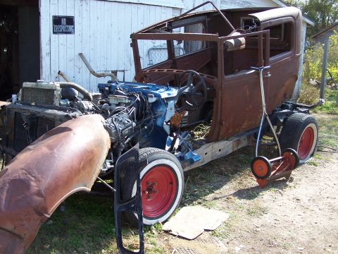 1995 Ford Bronco - A heavily rusted sedan chassis sits outdoors with its engine exposed and front fender removed, next to a building with a "NO TRESPASSING" s…