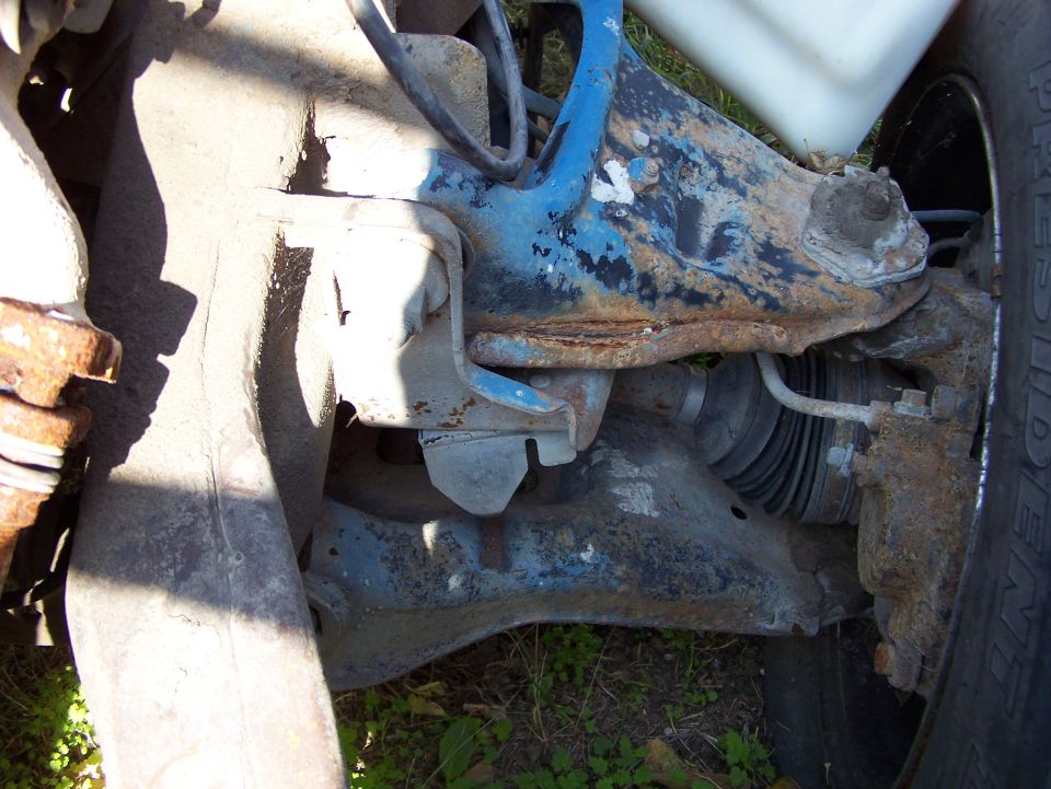 Rusty blue and gray vehicle suspension parts with a tire visible on the right