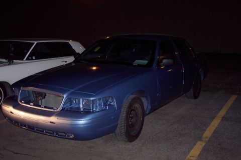 2001 Ford Crown Victoria - A blue 2001 Ford Crown Victoria is parked next to another vehicle, showing damage to its front end.