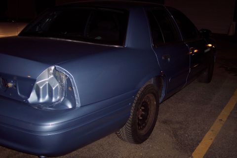 2001 Ford Crown Victoria - The rear of a blue sedan shows damage to the taillight area and a dented quarter panel.