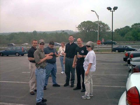 2000 Ford Crown Victoria - A group of individuals gathers in a parking lot, with multiple Ford Crown Victoria police vehicles parked nearby.