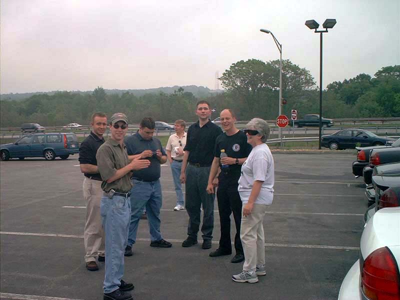 Group of people standing in a parking lot with several Ford Crown Victoria police cars visible