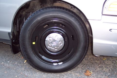2001 Ford Crown Victoria - Close-up of the front wheel and fender of a silver 2001 Ford Crown Victoria, a black steel wheel with a chrome Ford center cap.