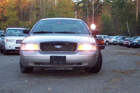 2001 Ford Crown Victoria - A silver 2001 Ford Crown Victoria is parked in a lot with its headlights illuminated.