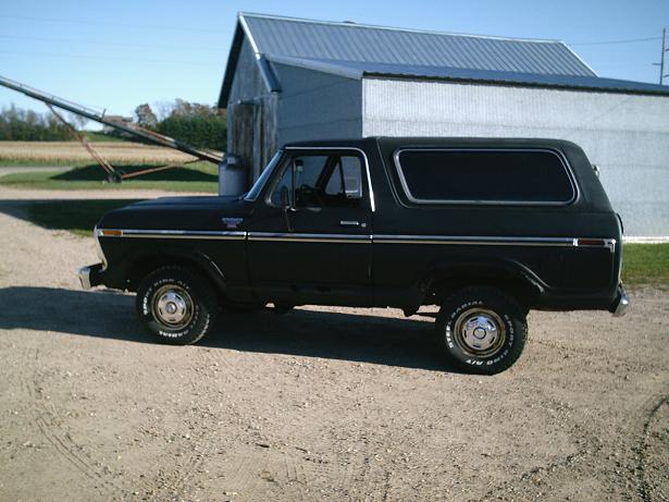 Black lifted late-1970s Ford Bronco with hardtop parked on dirt by a metal barn