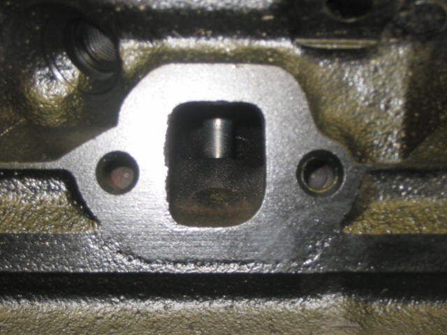 Close-up of a cylinder head exhaust port flange with bolt holes and machined surface