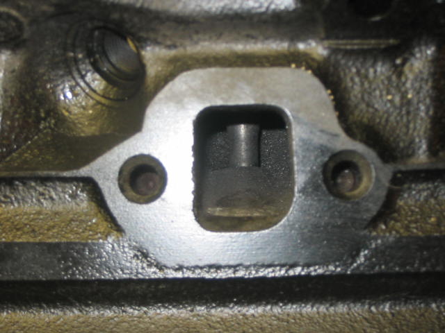 Close-up of exhaust port on cast iron cylinder head showing machined surface and bolt holes