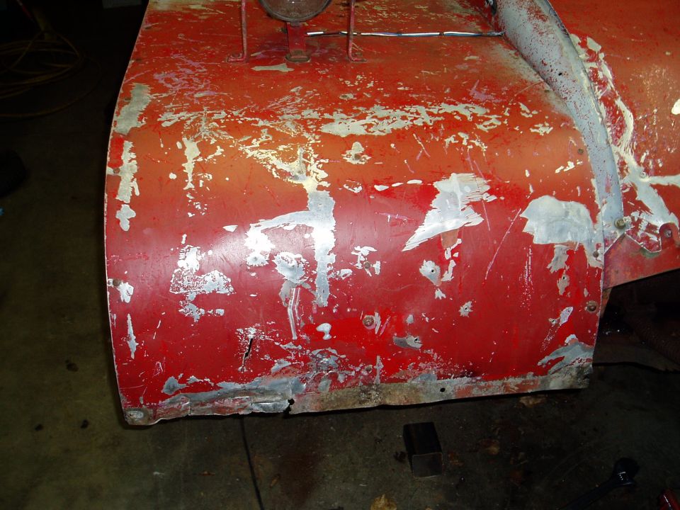 Close-up of a red snow blower housing with chipped paint and visible repairs