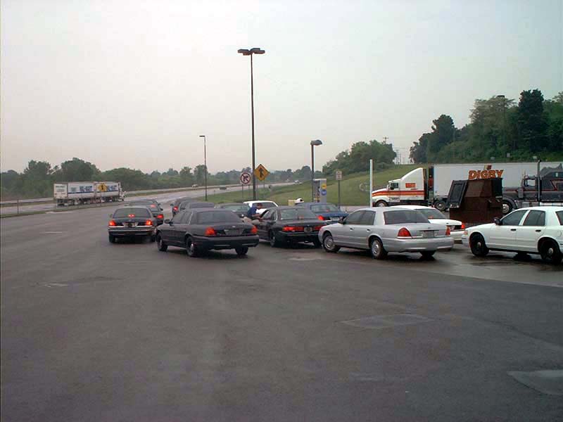 Several 2000 Ford Crown Victoria sedans parked on a wet road, with a semi-truck in the background
