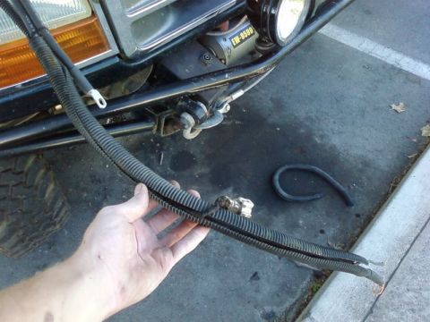 1995 Ford Bronco - A hand holds up long battery cables in black split-loom conduit with ring terminals and an inline connector, in front of a black truck's tu…