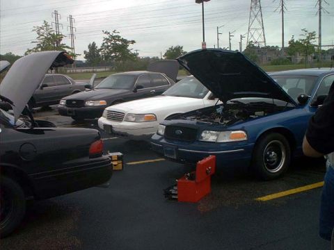 2000 Ford Crown Victoria - Multiple Ford Crown Victorias are parked together, with at least two having their hoods open, suggesting maintenance or repair work.